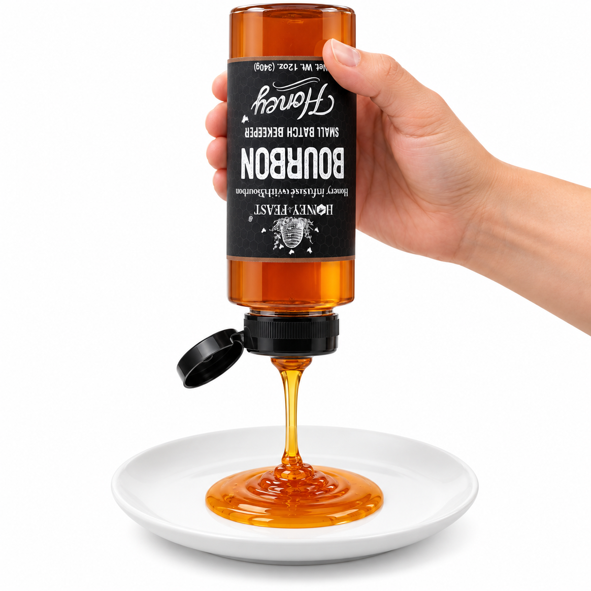 Hand squeezing an inverted Honey Feast Bourbon Honey 12oz plastic bottle onto a white plate with the flip-top lid open and label correctly upside down