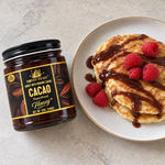 Honey Feast cacao honey 12oz glass jar beside pancakes topped with cacao honey and raspberries