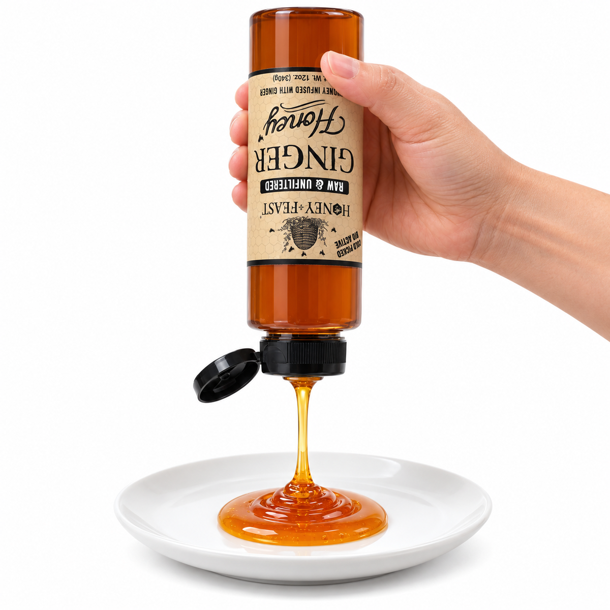 Hand squeezing an inverted Ginger Honey 12oz plastic bottle onto a white plate with the flip-top lid open and label correctly upside down