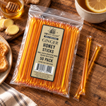 Ginger Honey Sticks 50-pack lying flat beside fresh ginger, honey and tea, with full-length loose sticks