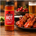 Honey Feast Hot Honey 12oz plastic bottle beside glazed chicken wings and chili peppers