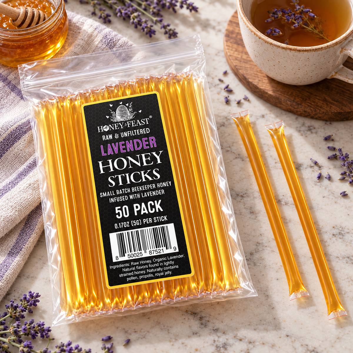 Honey Feast Lavender Honey Sticks 50-pack lying flat beside tea and lavender, with full-length loose honey sticks