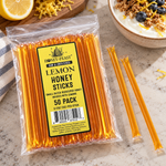 Honey Feast Lemon Honey Sticks 50-pack lying flat beside yogurt with granola, blueberries and lemon zest, with full-length loose sticks