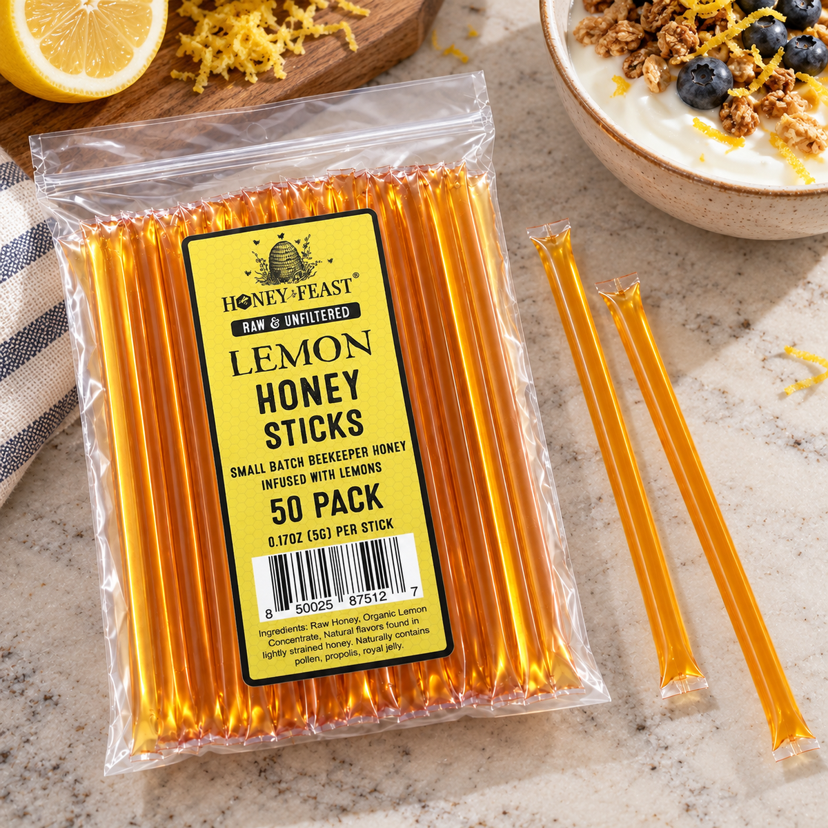 Honey Feast Lemon Honey Sticks 50-pack lying flat beside yogurt with granola, blueberries and lemon zest, with full-length loose sticks