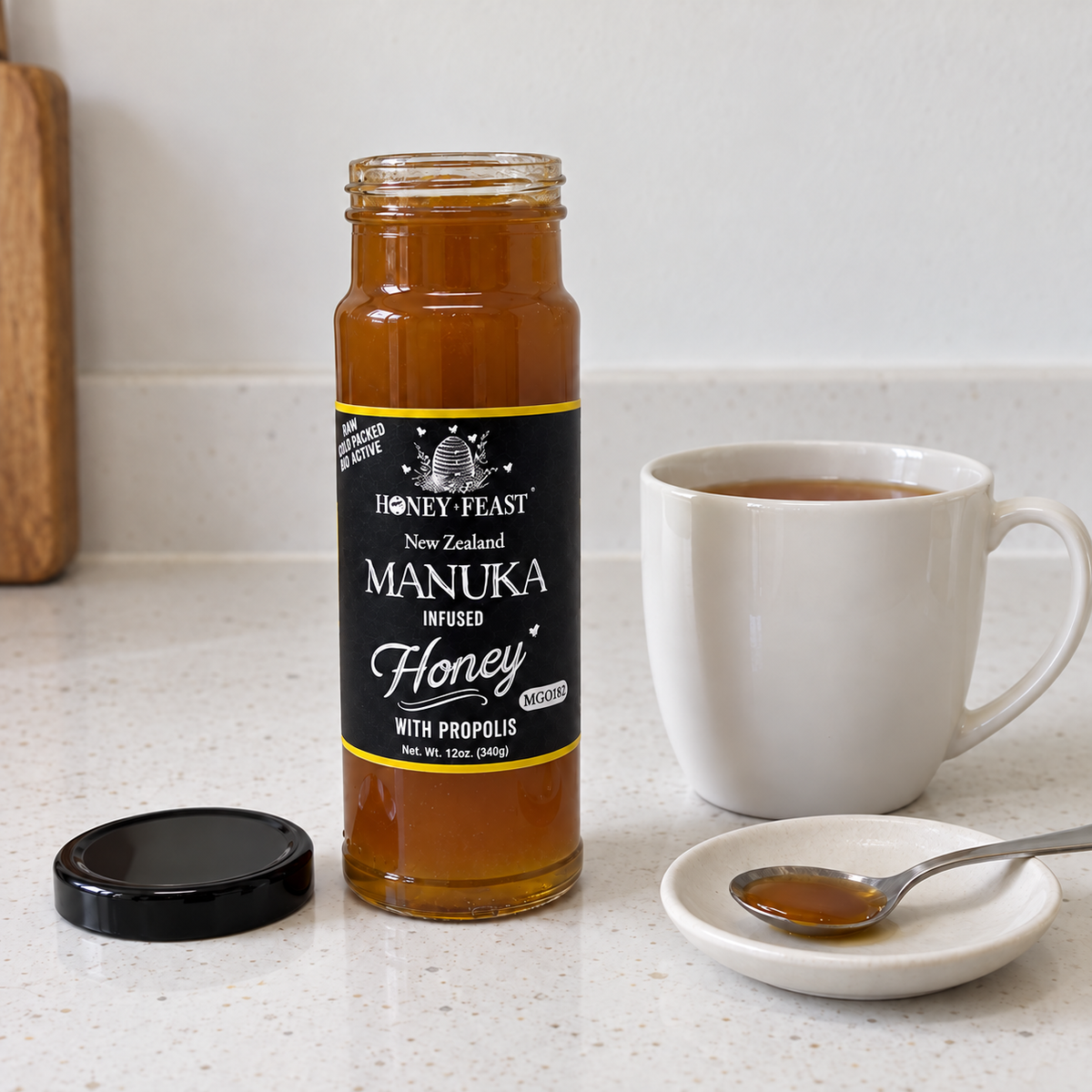 Honey Feast Manuka infused honey with propolis in a 12oz glass jar beside tea