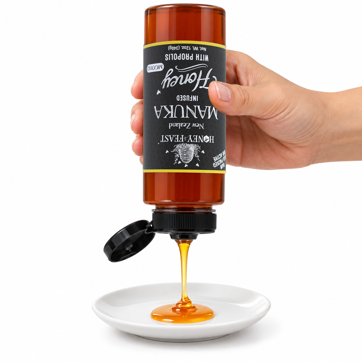 Hand squeezing an inverted 12oz plastic bottle of Honey Feast Manuka Infused Honey with Propolis onto a small white plate, with the original label upside down and the flip-top cap open