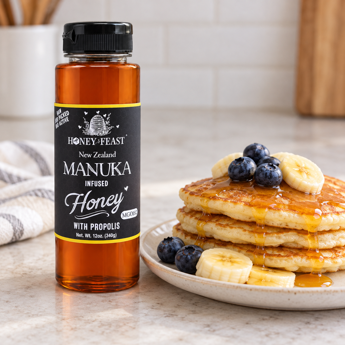 Honey Feast Manuka Infused Honey with Propolis 12oz plastic squeeze bottle beside pancakes with banana, blueberries and honey