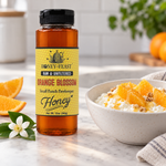 Honey Feast Orange Blossom Honey 12oz plastic squeeze bottle with its original yellow label beside a breakfast bowl with orange segments and honey