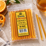 Orange Blossom Honey Sticks 50-pack lying flat beside tea and citrus, with full-length loose sticks