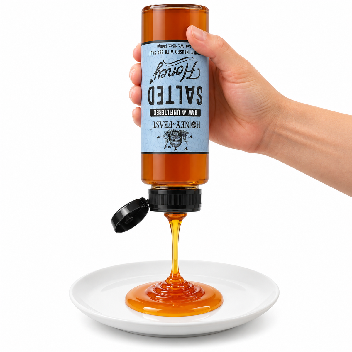 Hand squeezing an inverted Salted Honey 12oz plastic bottle onto a white plate with the flip-top lid open and label correctly upside down