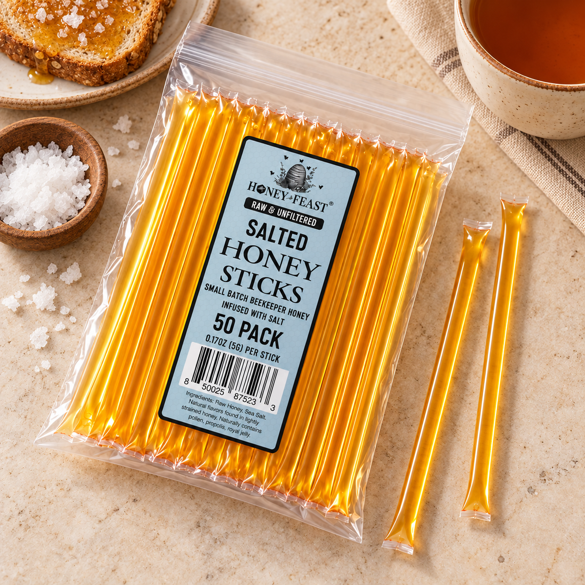 Salted Honey Sticks 50-pack lying flat beside sea salt, toast and tea with full-length loose sticks