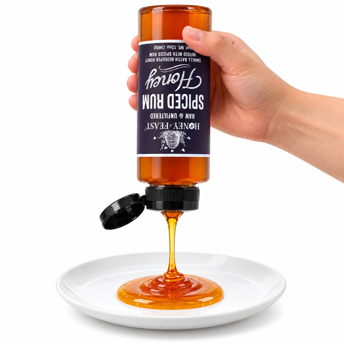 Hand squeezing an inverted Spiced Rum Honey 12oz plastic bottle onto a white plate with the flip-top lid open and label correctly upside down