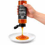 Hand squeezing an inverted Truffle Honey 12oz plastic bottle onto a white plate with the flip-top lid open and label correctly upside down