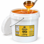 Open Honey Feast Black Gum Tupelo Honey 2-gallon bucket, with honey pouring from a stainless steel ladle on a white background.