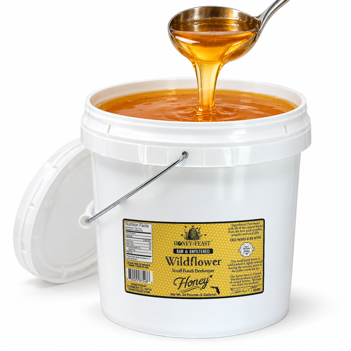 Open Honey Feast Wildflower Honey 2-gallon bucket with golden honey flowing from a stainless steel ladle, on a white background.